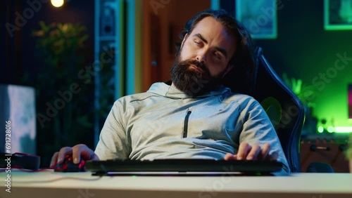 Gamer having seizure while at computer desk, exhausted after pathologically playing videogames all day. Lethargic man falling asleep, crashing with chair from fatigue, suffering from gaming addiction photo