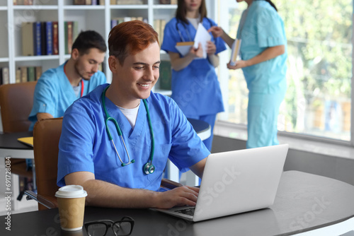 Male medical student studying with laptop in library