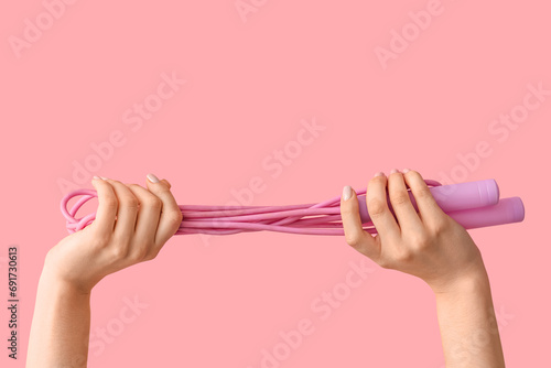 Female hands with skipping rope on pink background photo