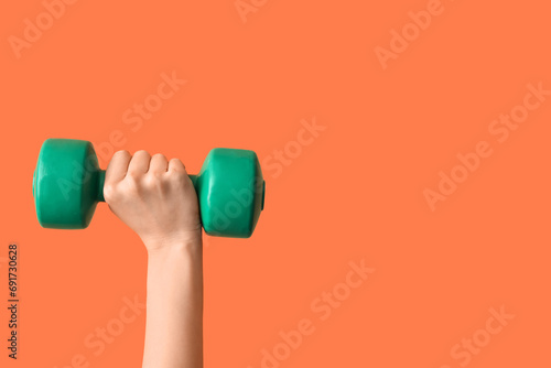 Female hands with dumbbell on orange background photo
