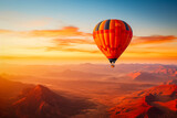A colorful hot air balloon floats in sky over a desert mountain landscape at sunset with orange and blue skies in the background. Travel journey adventure beauty of nature concept