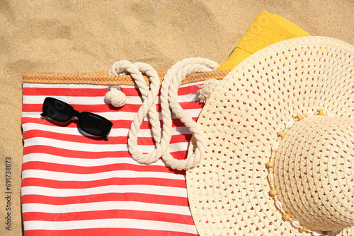 Striped beach bag, sunglasses, towel and hat on sand, flat lay photo