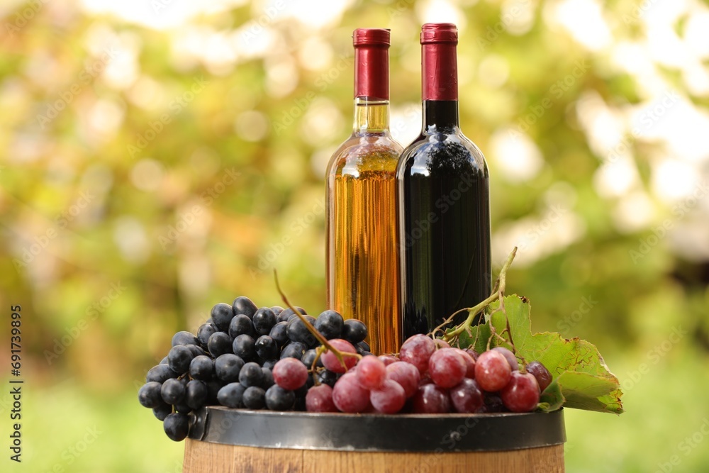 Delicious wines and ripe grapes on wooden barrel outdoors, space for text