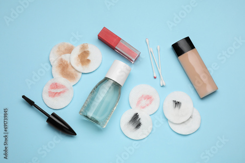 Bottle of makeup remover, dirty cotton pads, buds and different cosmetic products on light blue background, flat lay