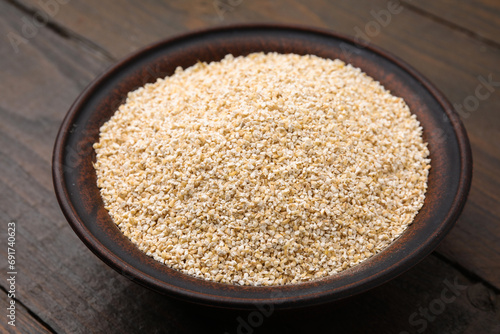 Raw barley groats in bowl on wooden table, closeup