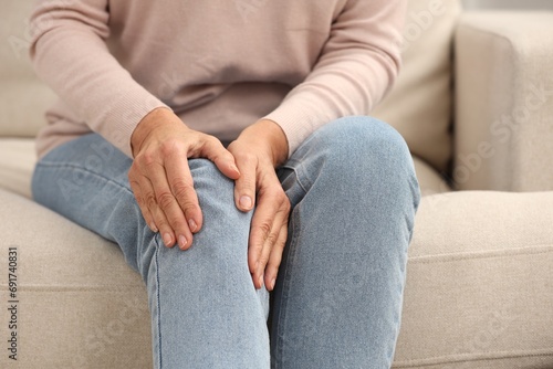 Mature woman suffering from knee pain on sofa, closeup. Rheumatism symptom