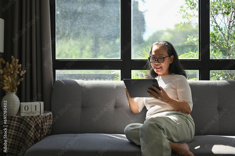 Cheedul middle age woman in casual clothes browsing internet on digital tablet at home Cheedul middle age woman in casual clothes browsing internet on digital tablet at home