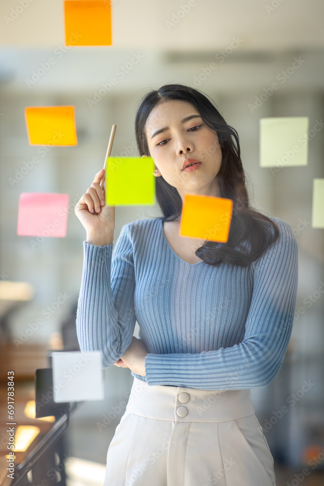 Happy asian businesswoman planning new project with sticky note in a creative writing on blank office glass Happy asian businesswoman planning new project with sticky note in a creative writing on blank office glass