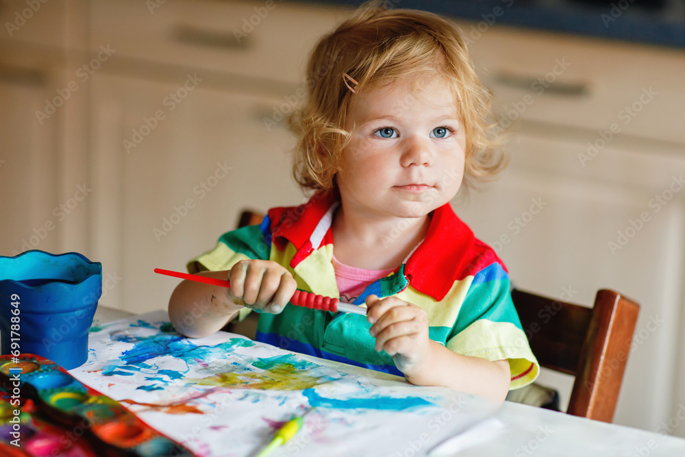 Cute adorable baby girl learning painting with water colors. Little toddler child drawing at home, using colorful brushes. Healthy happy daughter experimenting with colors, water at home or nursery. Cute adorable baby girl learning painting with water colors. Little toddler child drawing at home, using colorful brushes. Healthy happy daughter experimenting with colors, water at home or nursery.