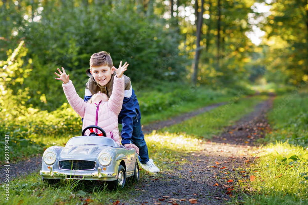 Two happy children playing with big old toy car in autumn forest, outdoors. Kid boy pushing and driving car with little toddler girl, cute sister inside. Laughing and smiling kids. Lovely family Two happy children playing with big old toy car in autumn forest, outdoors. Kid boy pushing and driving car with little toddler girl, cute sister inside. Laughing and smiling kids. Lovely family