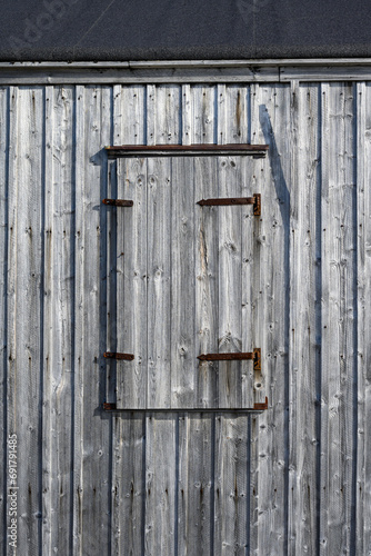 Weathered wooden siding with a closed window shutter, as a rustic background 