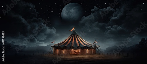 Spooky old circus tent under a large moon at night.