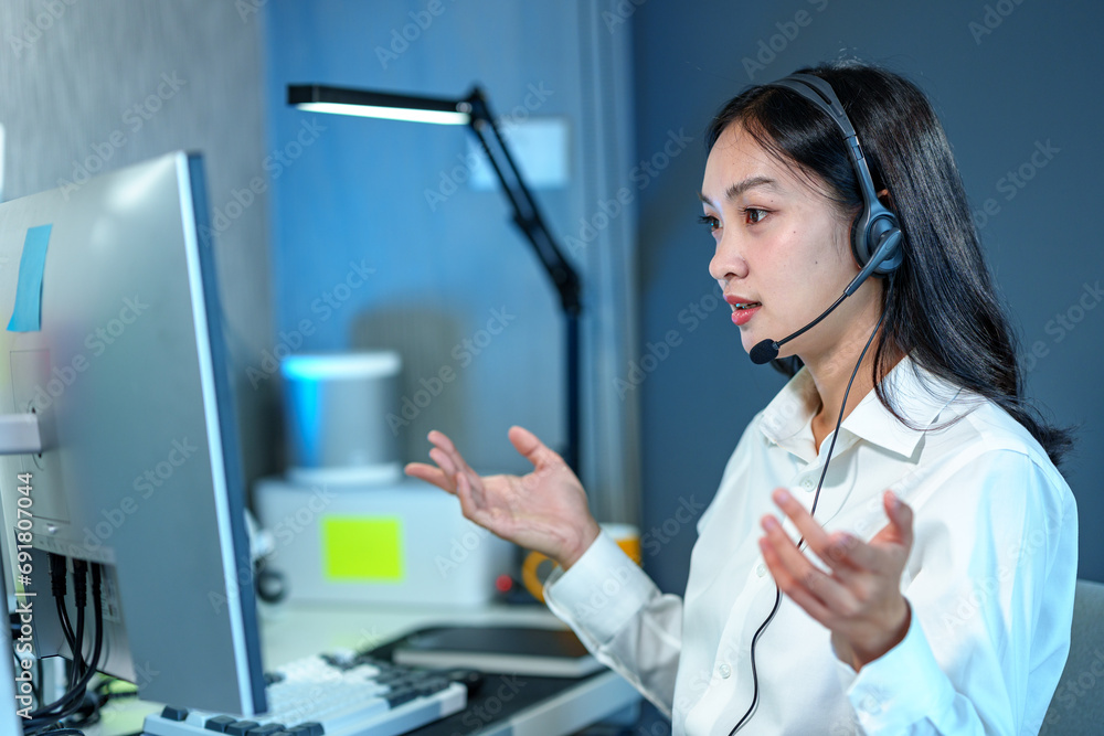 Young Asian call center woman working in a company. Attractive office worker sitting at a desk, wearing a headset and using a PC to talk to support customers, answer questions, explain information. Young Asian call center woman working in a company. Attractive office worker sitting at a desk, wearing a headset and using a PC to talk to support customers, answer questions, explain information.