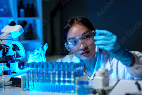 Medical scientist, researcher, lab assistant holding test tube through blue solution sample, doing chemical experiment and examining, comparing biological results, medical and research concept.