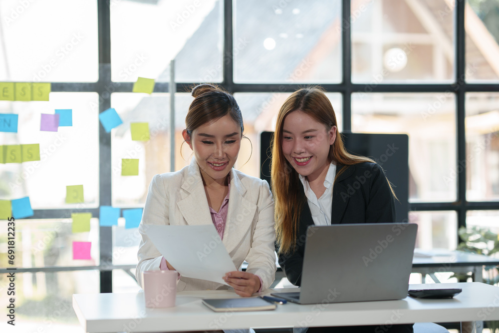 Two Asian businesswomen are discussing market data graphs and company data charts from folders, documents, new investment projects. and strategic planning using laptop computers in the office. Two Asian businesswomen are discussing market data graphs and company data charts from folders, documents, new investment projects. and strategic planning using laptop computers in the office.
