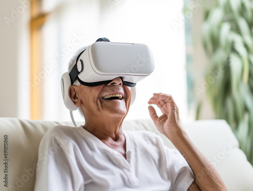 An elderly woman is sitting in the living room, wearing virtual reality glasses and smiling. Modern technology and the golden years. A photorealistic image.  © Mariia Mazaeva