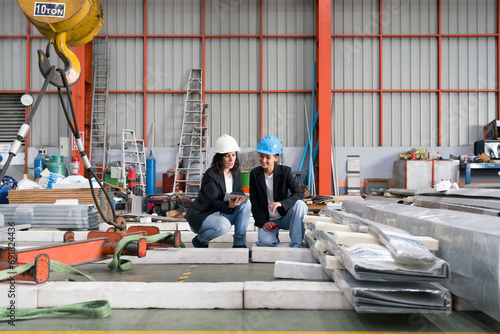 Two women wearing safety hats are energetically working together in a spacious and organized warehouse. © chadchai