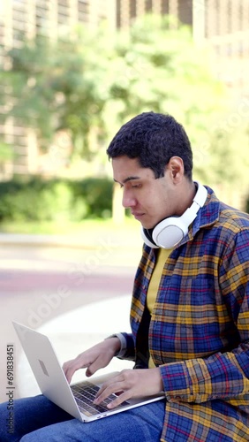Vertical slow motion video of a latin student using laptop gesturing success sitting outdoors the campus