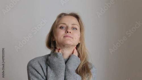 A young girl in a cozy gray sweater puts her hands on her neck and looks at the camera.