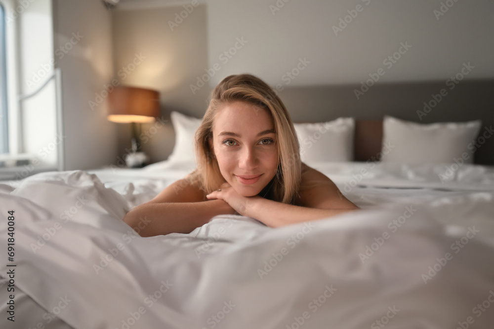 Young, inviting woman on hotel bed, relaxed and content
