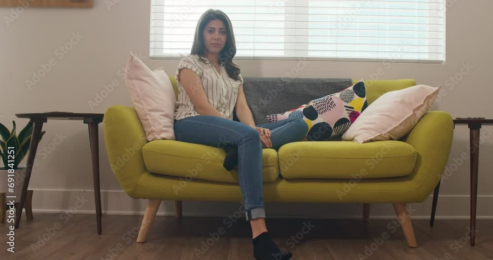 Portrait of millennial white woman sitting on couch in her living room looking at camera. Caucasian woman backlit by open window in contemporary living room. 4k slow motion handheld Portrait of millennial white woman sitting on couch in her living room looking at camera. Caucasian woman backlit by open window in contemporary living room. 4k slow motion handheld
