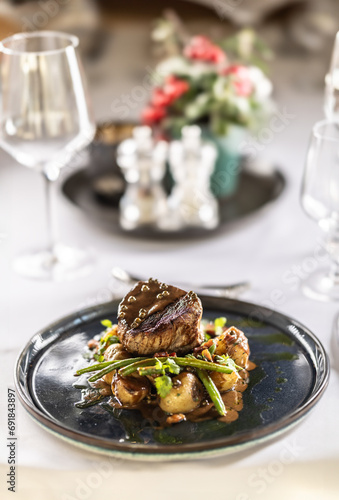Fillet steak from beef tenderloin, sautéed green beans with bacon, baked potatoes and green pepper sauce. Fillet steak served on a plate on a festive table in a restaurant