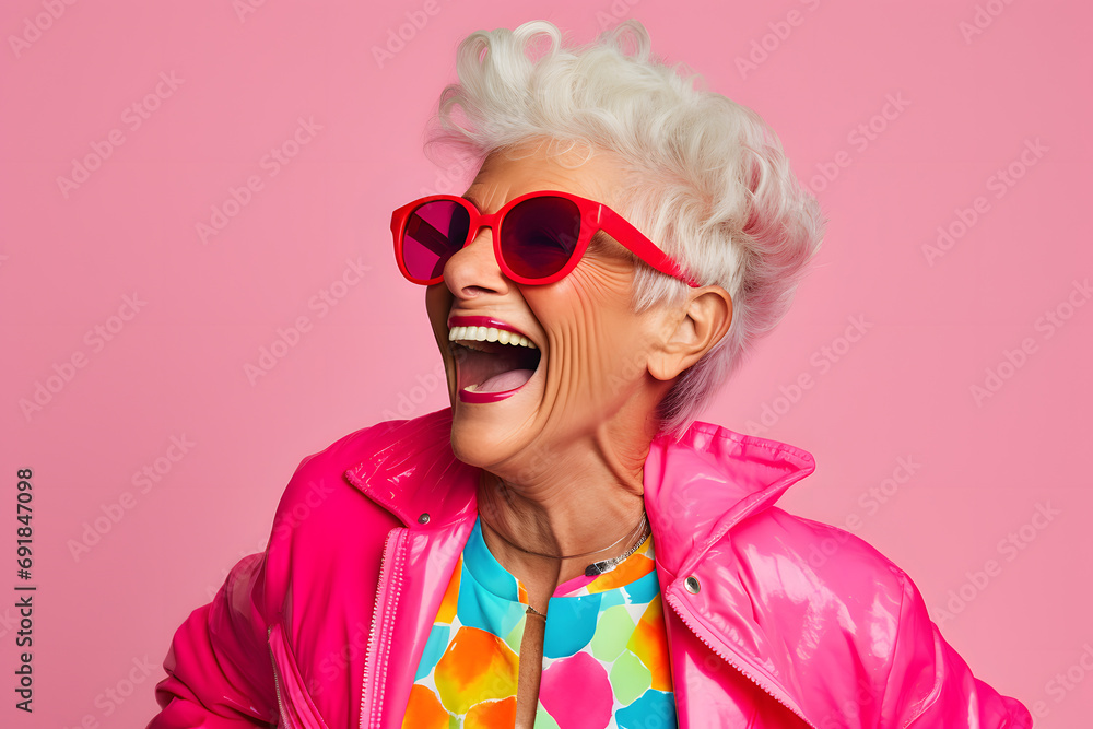 Elderly woman in colorful clothes with sunglasses in front of pink studio background