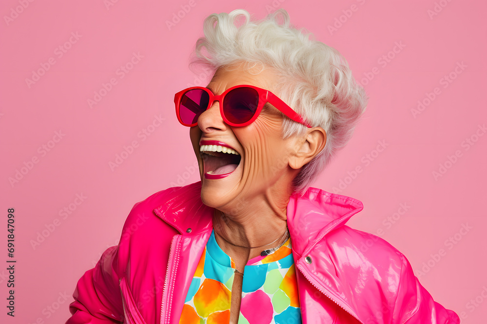 Elderly woman in colorful clothes with sunglasses in front of pink studio background Elderly woman in colorful clothes with sunglasses in front of pink studio background