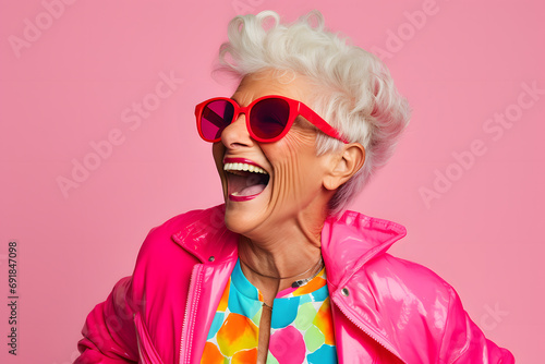 Elderly woman in colorful clothes with sunglasses in front of pink studio background