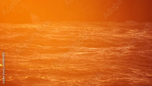 Storm Wave Sunset. Storm wave approaching the coast at golden burning sunset with spray originated by wind in backlight. Seascape with large breaking waves. Weather and climate change photo