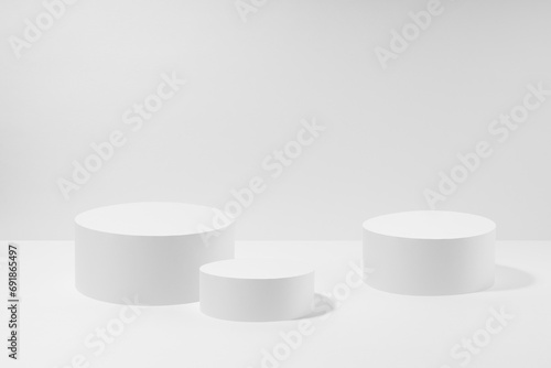 Abstract three white round podiums for cosmetic products in hard light, mockup on white background. Scene for presentation products, gifts, goods, advertising, design, sale, display in minimal style.