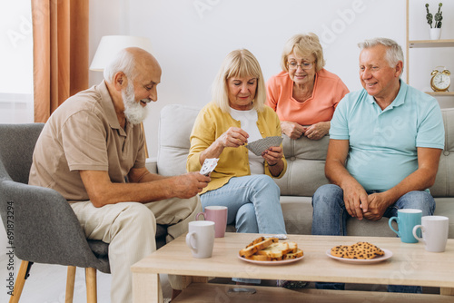 Group of senior people laughing while relaxing at home and playing cards.