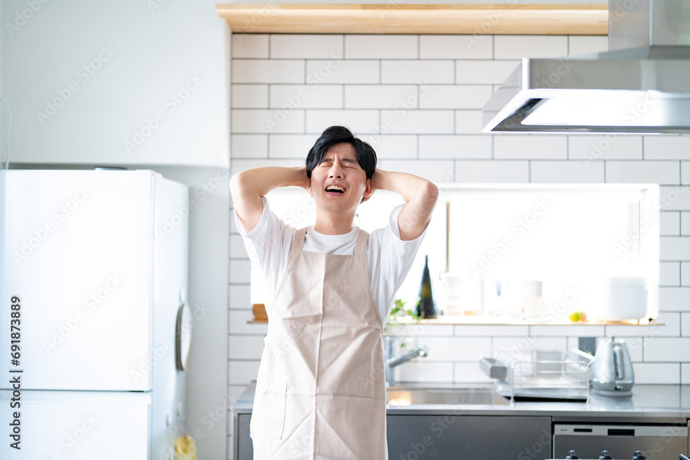 頭を抱えるエプロンをつけた若い日本人男性 頭を抱えるエプロンをつけた若い日本人男性