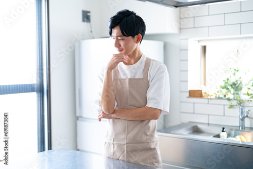 キッチンで考えるエプロンをつけた若い日本人男性