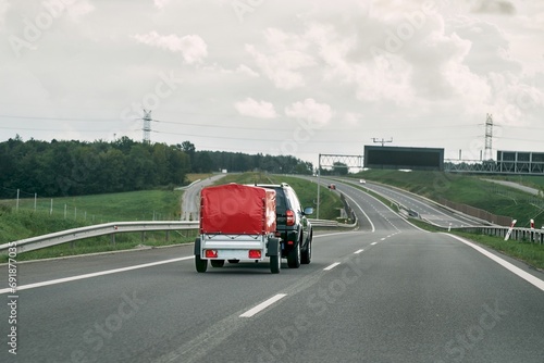SUV with trailer goes on the highway. Moving stuff with a small rentable trailer.