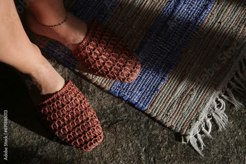 Woman standing in handmade raffia mules on the striped handwoven wool rug. Sustainable ethically made pair of slippers. Responsibly sourced shoes with eco-friendly materials. photo