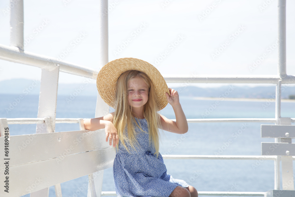 Adorable little girl in blue cotton dress and straw hat travelling on ferry, summer vacation travelling concept 