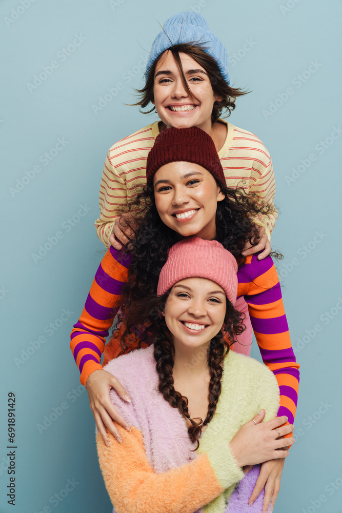 Portrait of three cheerful girls posing and hugging while standing isolated over blue studio background Portrait of three cheerful girls posing and hugging while standing isolated over blue studio background