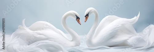 A duo of graceful swan sculptures creating a heart silhouette against gently folded silk cloth photo