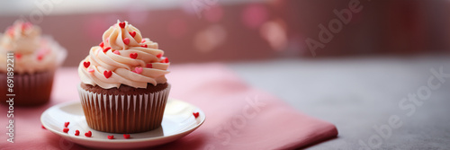 A dainty cupcake topped with a heart shape decoration on a plain, solid hued plate