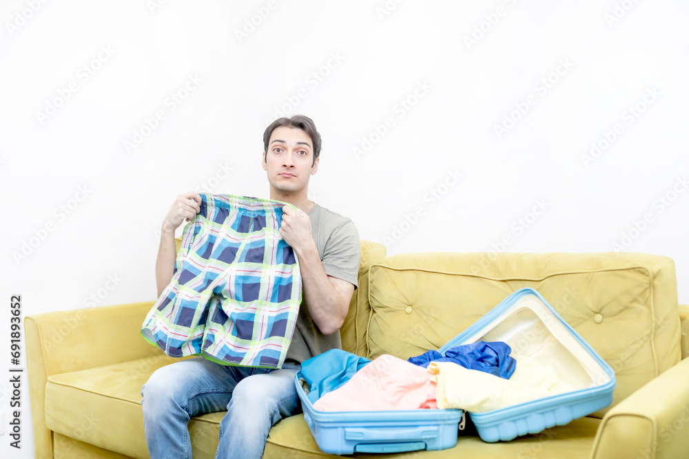 Young man sits on sofa and packs a suitcase for vacation Young man sits on sofa and packs a suitcase for vacation