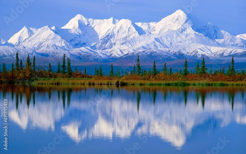 the snow covered mountains reflected in the water and the trees near by