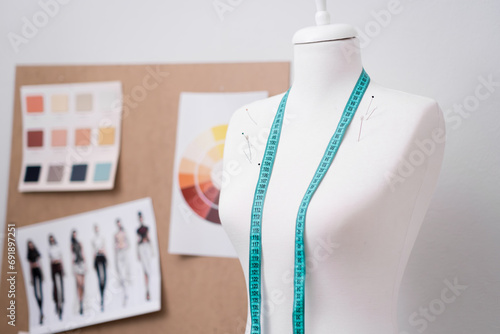 Tape measure and pins on dummy near corkboard with swatches and sketches in dressmaking shop clothes sewing equipment in contemporary atelier empty tailor studio photo