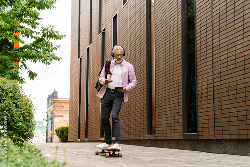 Senior man using tablet riding skateboard outdoors photo
