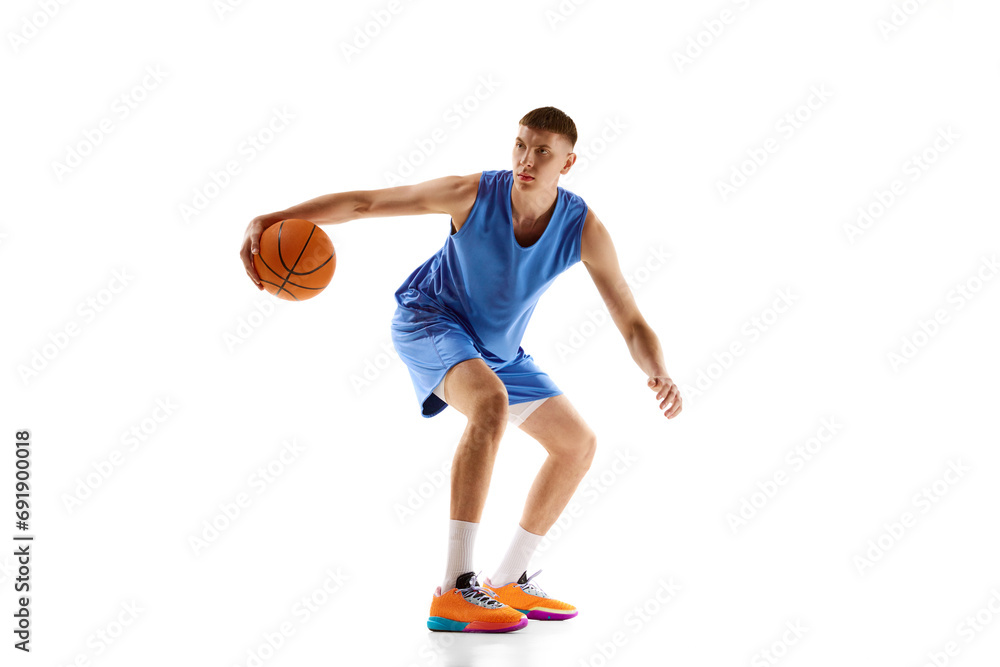 Concentrated young man in blue uniform, basketball player in motion, playing with ball isolated over white background. Professional sport, competition, match, championship, health, action concept. Ad