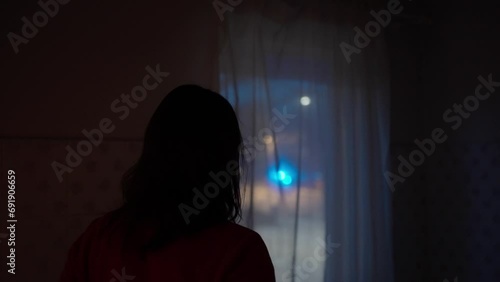 Woman looks out the window of her house observing night incident scene with out of focus police lights photo
