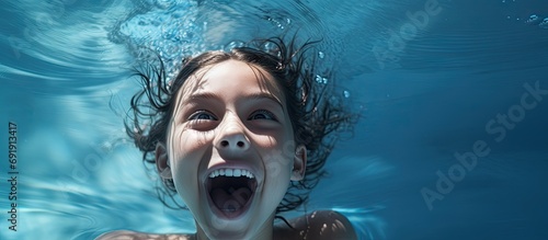A tween girl in a swimming pool covers her mouth with her hand She is embarrassed to have her crooked teeth show in pictures She looks a bit surprised or scared. Copy space image photo
