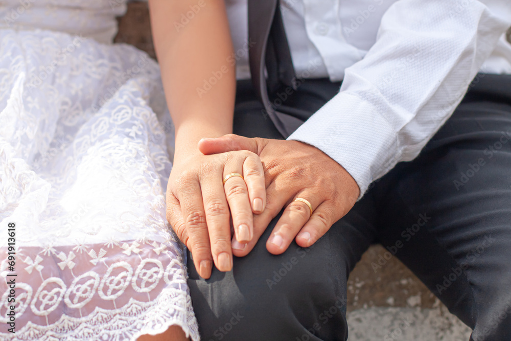 Obraz premium Hands of bride and groom holding together with wedding rings