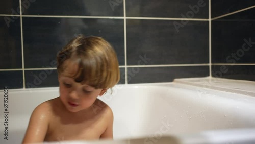 Child plays with car toy inside bathtub. One small boy enjoying bath-time night routine before bedtime photo
