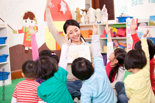 Cute kindergarten children raising hands to answer female teacher's question photo